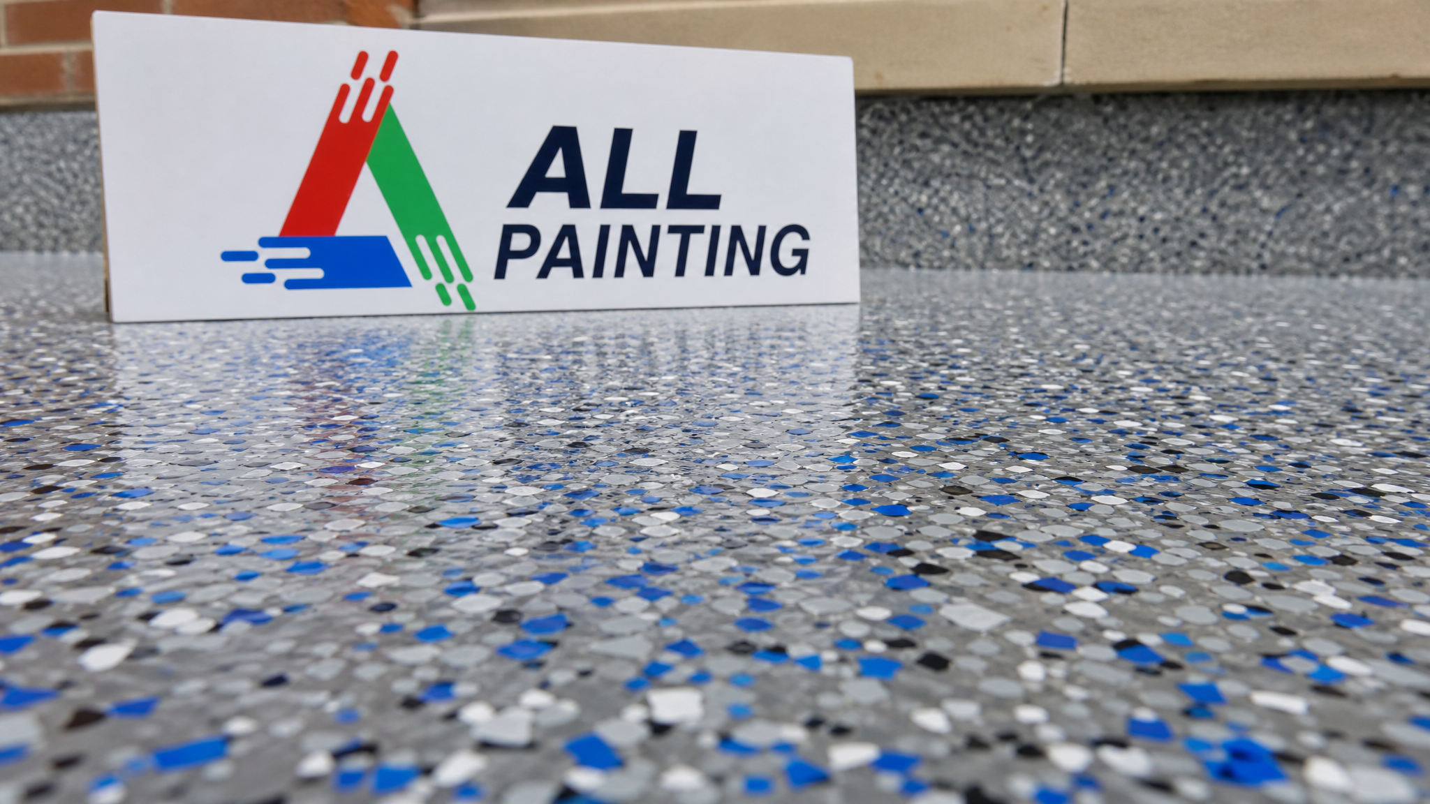 Close-up of decorative colour flakes broadcast into a clear-coated epoxy garage floor with a small All Painting sign placard